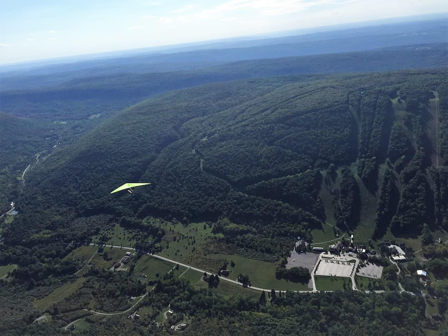 A hang glider soaring over Bristol Mountain and the wooded valley, from the RAF club archive