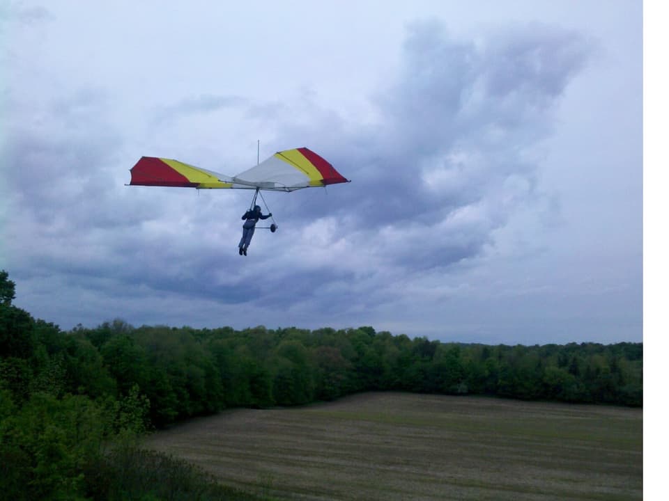 A hang glider above a tree-lined field, from the RAF club archive